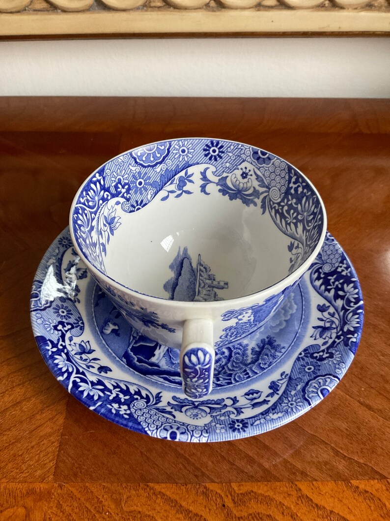 May include: A blue and white porcelain teacup and saucer set with a floral pattern. The cup and saucer feature a blue and white landscape scene with a castle.