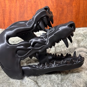 May include: A black, stylized sculpture of a canine skull, featuring detailed teeth and a textured surface. The sculpture is set against a backdrop of faux fur and a wooden panel.