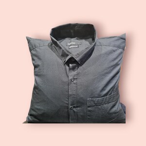 Pode incluir: Uma camisa preta de botões com padrão de bolinhas brancas. A camisa tem um bolso do lado esquerdo e uma gola de botões.
