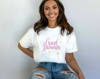 Puede incluir: Una camiseta blanca con el texto "Cruel Summer" en letra rosa con estrellas doradas.