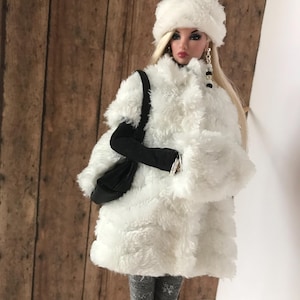 May include: A white faux fur coat with a white faux fur hat and a black handbag. The doll is wearing grey tights and white shoes.