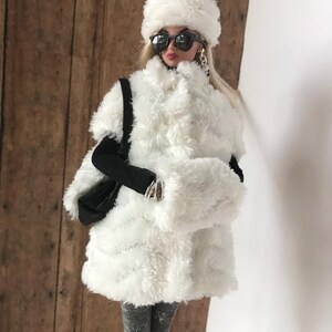 May include: A white faux fur coat with a white faux fur hat and black sunglasses. The coat has a long, loose fit and is perfect for winter.