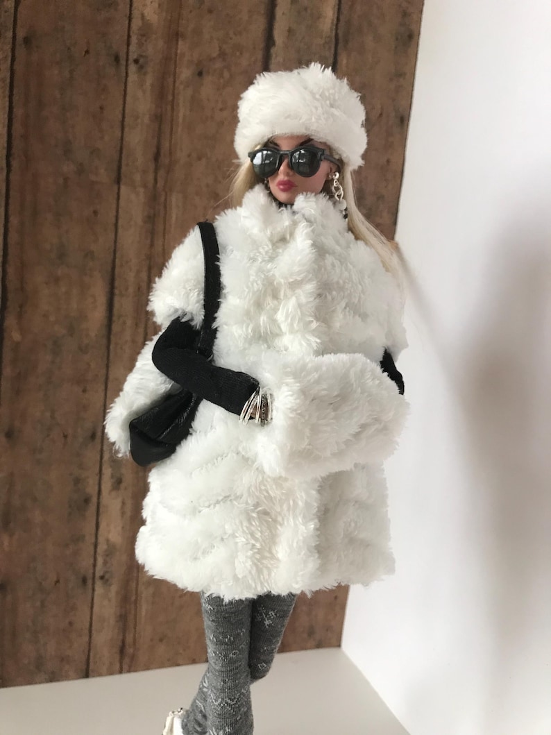May include: A white faux fur coat with a white faux fur hat and black sunglasses. The coat has a long, loose fit and is perfect for winter.