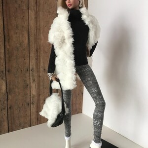 May include: A fashion doll wearing a white faux fur vest, a black turtleneck sweater, gray leggings with a snowflake pattern, and white boots. The doll is holding a white faux fur handbag with a black strap.