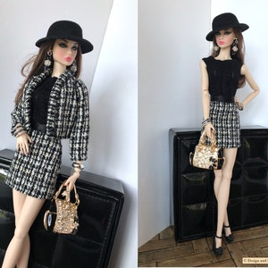 May include: A black and white checkered skirt and jacket set with a black top, black hat, and gold handbag. The doll is wearing black earrings and bracelets.