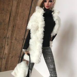 May include: A doll wearing a white faux fur vest, a black turtleneck sweater, gray leggings with a snowflake pattern, and white faux fur handbag.