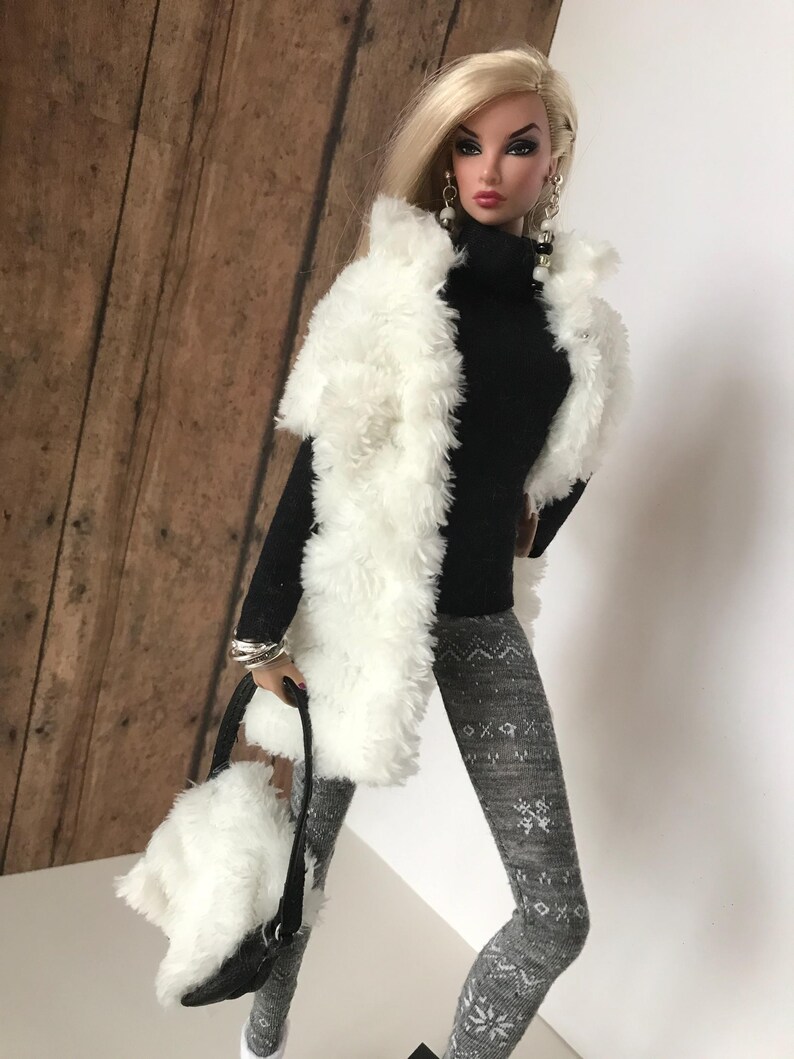 May include: A doll wearing a white faux fur vest, a black turtleneck sweater, gray leggings with a snowflake pattern, and white faux fur handbag.