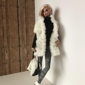 May include: A fashion doll wearing a white faux fur vest, a black turtleneck sweater, gray patterned leggings, and white ankle boots. The doll is holding a white faux fur handbag with a black strap.