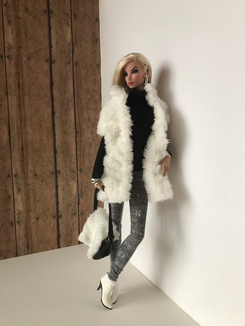 May include: A fashion doll wearing a white faux fur vest, a black turtleneck sweater, gray patterned leggings, and white ankle boots. The doll is holding a white faux fur handbag with a black strap.