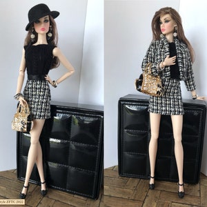 May include: A fashion doll wearing a black and white checkered skirt and a black top with a black hat. The doll is holding a gold and black handbag. The doll is standing on a black surface. The image includes the text "Z French Touch Couture".