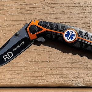 May include: A black folding knife with an orange handle and a black and orange patterned handle. The knife has a medical symbol on the handle and the text "RD TAC-FORCE" on the blade.