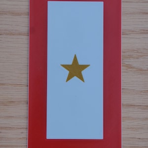 May include: A red framed white card with a gold star in the center. The card is a military rank insignia.
