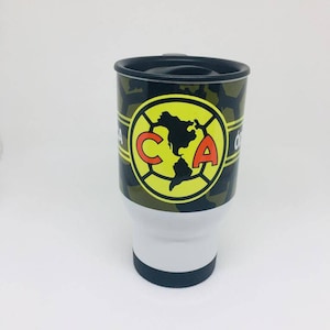 May include: A white travel mug with a black lid and a camouflage pattern. The mug has a yellow circle with a red "CA" logo and a black outline. The logo features a map of North America.