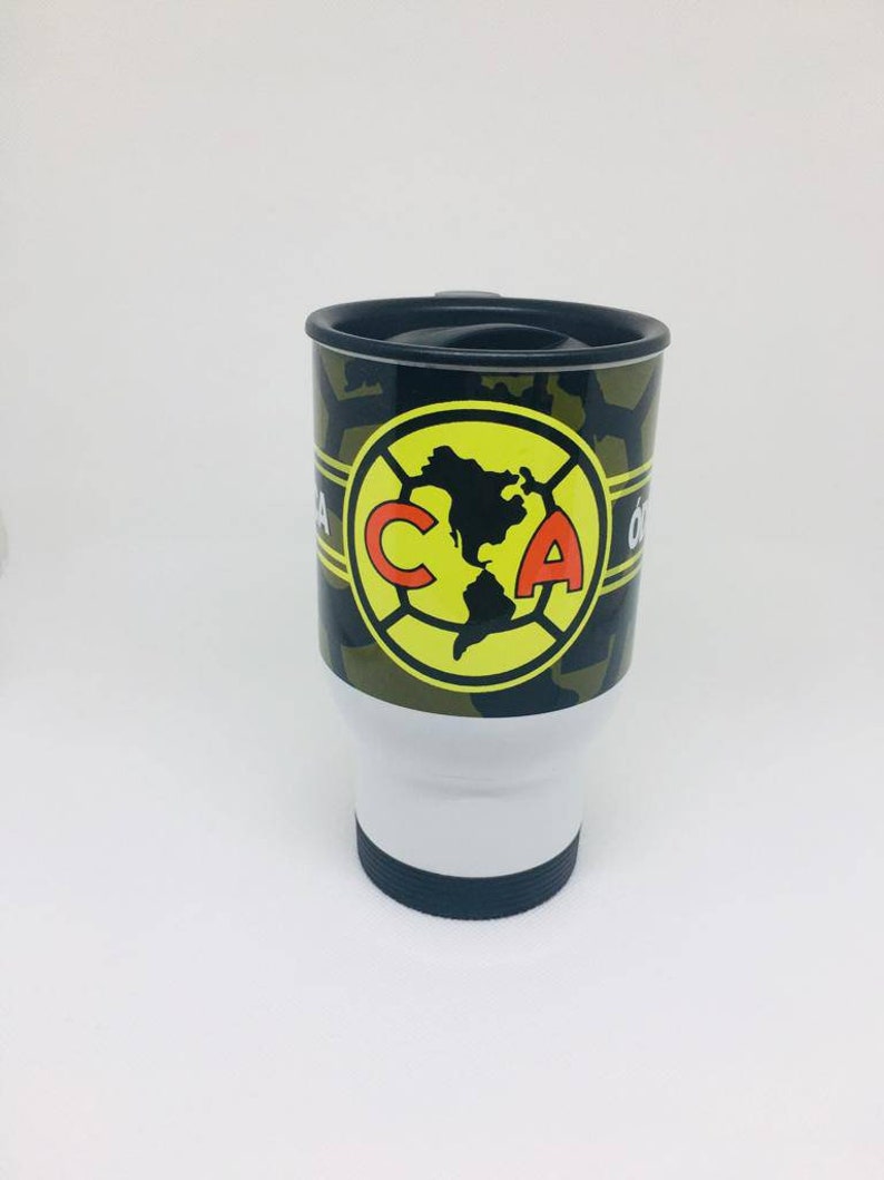 May include: A white travel mug with a black lid and a camouflage pattern. The mug has a yellow circle with a red "CA" logo and a black outline. The logo features a map of North America.
