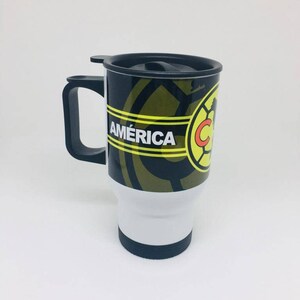 May include: A black and gold travel mug with a black lid and handle. The mug has a white stripe with the word "AM&Eacute;RICA" in yellow letters and a soccer ball logo with the letter "C" in red.