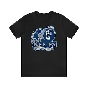 Może przedstawiać: Czarny T-shirt z niebiesko-szarym nadrukiem przedstawiającym lwa w koronie. Nadruk głosi "Oh Kee Pa Ceremony".