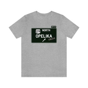 Puede incluir: Una camiseta gris con una señal de carretera en blanco y negro que dice "Salida 64 Norte 29 Opelika Yella".
