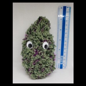 Pode incluir: Um brinquedo de pelúcia verde e roxo com olhos saltados. O brinquedo tem aproximadamente 18 cm de altura e está ao lado de uma régua.