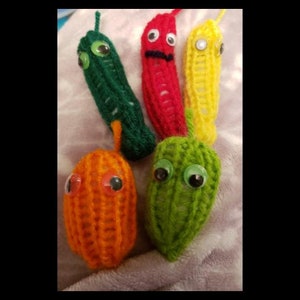 Pode incluir: Cinco fantoches de dedo de crochê com formato de vegetais. Os fantoches são verdes, vermelhos, amarelos e laranja. Cada fantoche tem olhos saltados.