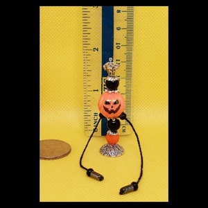 May include: A miniature Halloween-themed candle holder with a black and orange pumpkin design. The holder is made of beads and metal and has a black cord.