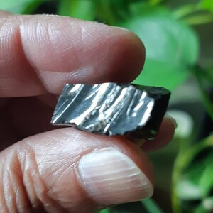 K&ouml;nnte beinhalten: Ein dunkelgrauer, metallischer Meteorit mit einer rauen, strukturierten Oberfl&auml;che. Der Meteorit hat ein einzigartiges, gestreiftes Muster.