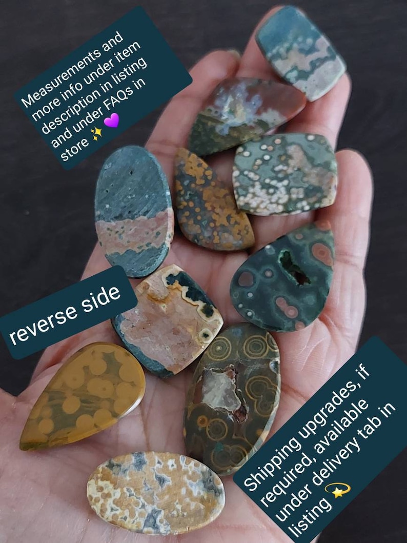 May include: A collection of eight green, brown, and white ocean jasper cabochons with various patterns. The cabochons are displayed on a hand.