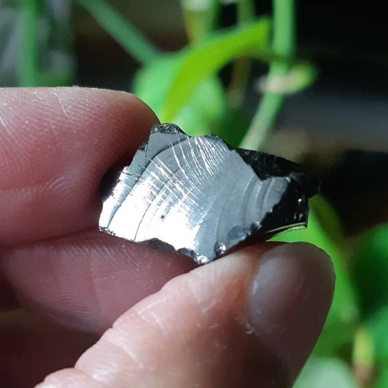 K&ouml;nnte beinhalten: Ein unregelm&auml;&szlig;ig geformter, dunkelgrauer, metallischer Stein mit einer silbrigen, gestreiften Oberfl&auml;che.