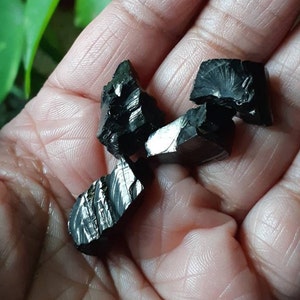 K&ouml;nnte beinhalten: Eine Sammlung von f&uuml;nf schwarzen Obsidian-Kristallen mit einem metallischen Schimmer. Die Kristalle sind unregelm&auml;&szlig;ig geformt und haben scharfe Kanten.