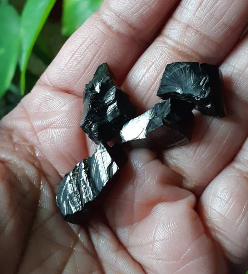 K&ouml;nnte beinhalten: Eine Sammlung von f&uuml;nf schwarzen Obsidian-Kristallen mit einem metallischen Schimmer. Die Kristalle sind unregelm&auml;&szlig;ig geformt und haben scharfe Kanten.