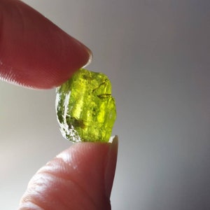 Könnte beinhalten: Ein grüner Peridot-Kristall mit rauer, natürlicher Textur. Der Kristall ist durchscheinend und hat einen leichten Gelbstich.