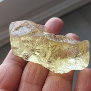 K&ouml;nnte beinhalten: Ein gro&szlig;er, rauer, durchscheinender, gelb-goldener Kristall mit einer glatten, polierten Oberfl&auml;che. Der Kristall hat ein nat&uuml;rliches, rohes Aussehen.