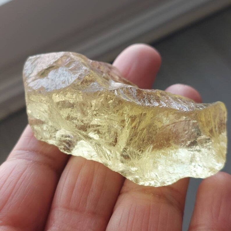 K&ouml;nnte beinhalten: Ein gro&szlig;er, rauer, durchscheinender, gelb-goldener Kristall mit einer glatten, polierten Oberfl&auml;che. Der Kristall hat ein nat&uuml;rliches, rohes Aussehen.