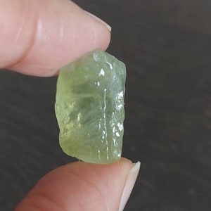 May include: A light green, translucent, faceted gemstone. The gemstone is irregularly shaped and has a rough, natural finish.