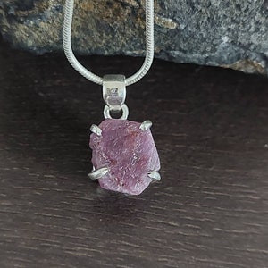 May include: A silver chain necklace with a pendant featuring a raw pink ruby gemstone set in silver.