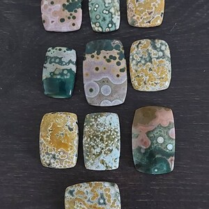 May include: Ten polished, rectangular, ocean jasper stones with a variety of colors and patterns, including green, brown, white, and yellow.