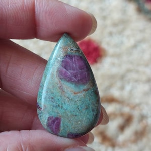 Op de afbeelding: Een traanvormige hanger van groene en roze edelsteen met een swirl-patroon en rode insluitsels.