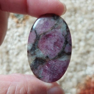 May include: Oval shaped pink and black gemstone cabochon. The stone has a swirling pattern of pink and black.
