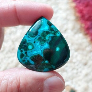 May include: A teardrop-shaped cabochon of turquoise green and blue chrysocolla with a swirling pattern and white inclusions.