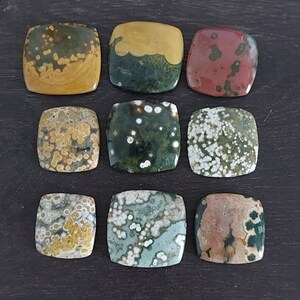 May include: Ten square-shaped polished stones with a variety of colors and patterns, including green, brown, yellow, and white. The stones have a speckled appearance.