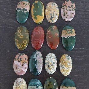 May include: A collection of 18 oval-shaped ocean jasper stones with various patterns and colors, including green, brown, red, white, and yellow.