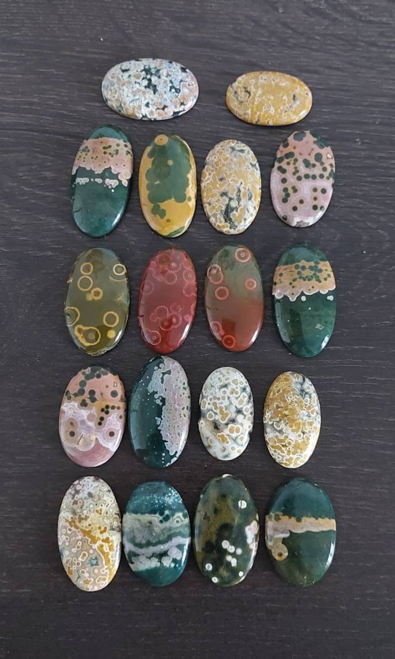 May include: A collection of 18 oval-shaped ocean jasper stones with various patterns and colors, including green, brown, red, white, and yellow.