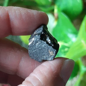 K&ouml;nnte beinhalten: Ein schwarzer, rauer und unregelm&auml;&szlig;ig geformter Stein mit einem leicht metallischen Schimmer.
