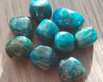 May include: A collection of eight blue apatite tumbled stones. The stones are smooth and polished, with a variety of shades of blue.