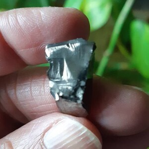 K&ouml;nnte beinhalten: Nahaufnahme eines kleinen, dunkelgrauen, metallischen Meteoriten mit einer rauen, strukturierten Oberfl&auml;che.