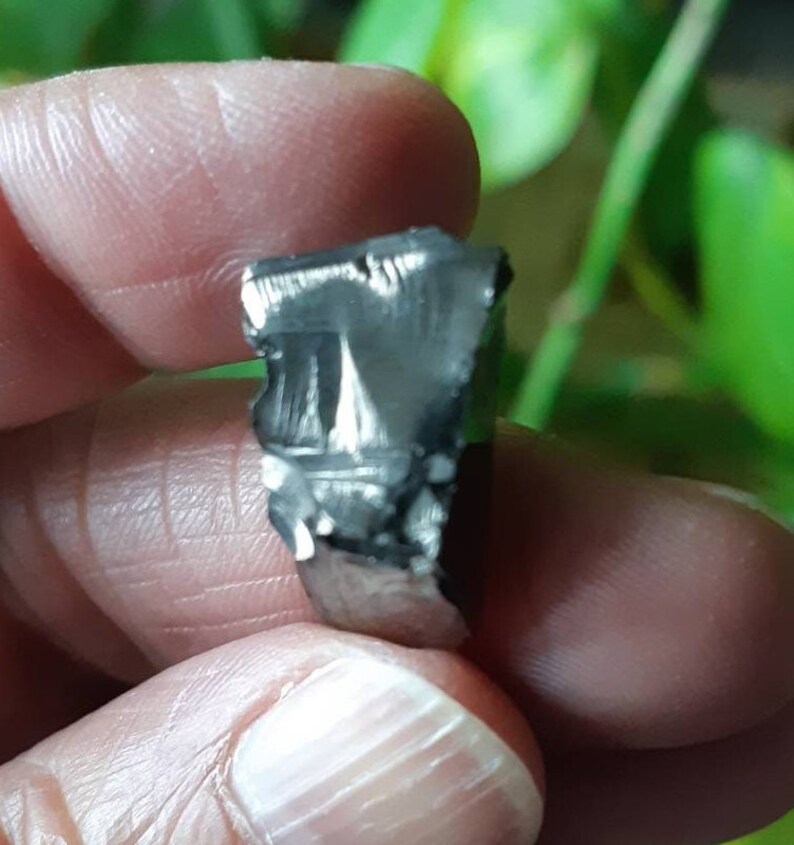 K&ouml;nnte beinhalten: Nahaufnahme eines kleinen, dunkelgrauen, metallischen Meteoriten mit einer rauen, strukturierten Oberfl&auml;che.