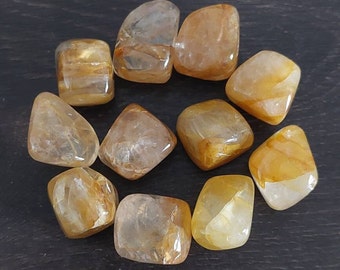 May include: A collection of ten tumbled citrine stones, each with a unique shape and size. The stones are a light yellow color with a translucent appearance.