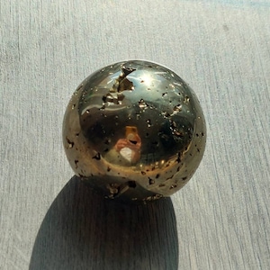 May include: A golden pyrite sphere with a rough, textured surface. The sphere reflects light, creating a shimmering effect.