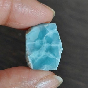 May include: A light blue, irregularly shaped piece of blue calcite with white veins. The stone is translucent and has a smooth, polished surface.