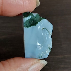 May include: A light blue and green agate stone with a rough, irregular shape. The stone has a translucent appearance with a white centre and green accents.