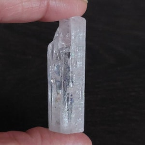 May include: A clear, faceted, crystal prism with a slightly pink hue. The prism is about 2 inches long and has a rectangular shape.